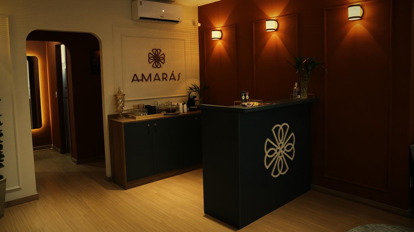 Recepção de uma unidade Amarás Spa à noite: parede terracota, letreiro Amarás e balcão com a mandala
